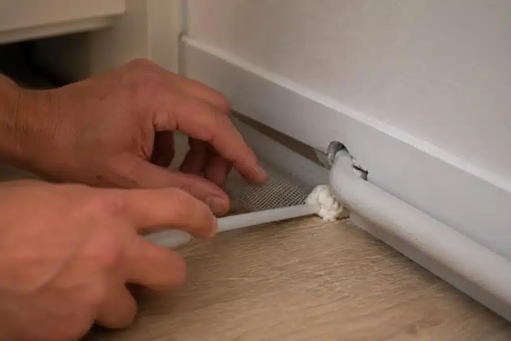 Hände, die einen Spalt am Mauerfuss mit Gitter und Schaum abdichten, nach der Nagerbekämpfung