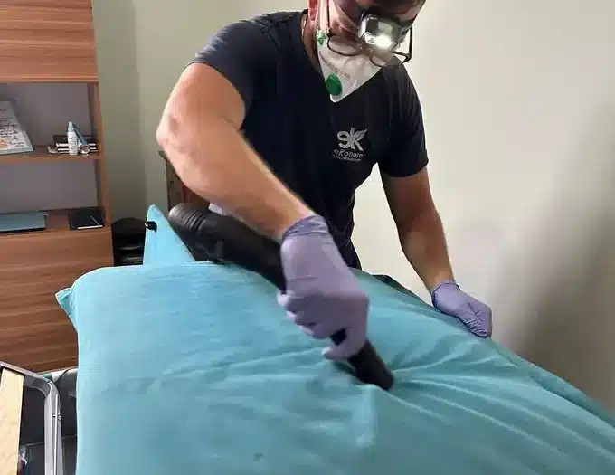 Tecnico Ekonore ispeziona e aspira un materasso con lampada frontale durante la disinfestazione delle cimici dei letti