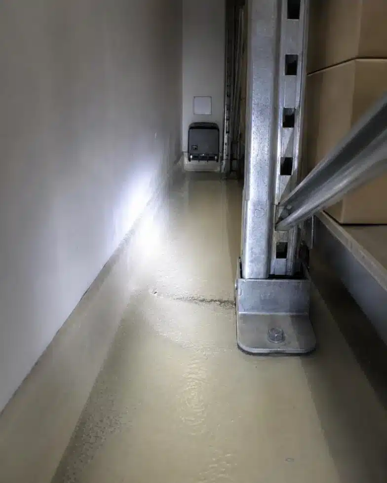 Fessura fra scaffale industriale e muro con tracce sul pavimento e postazione di monitoraggio numerata