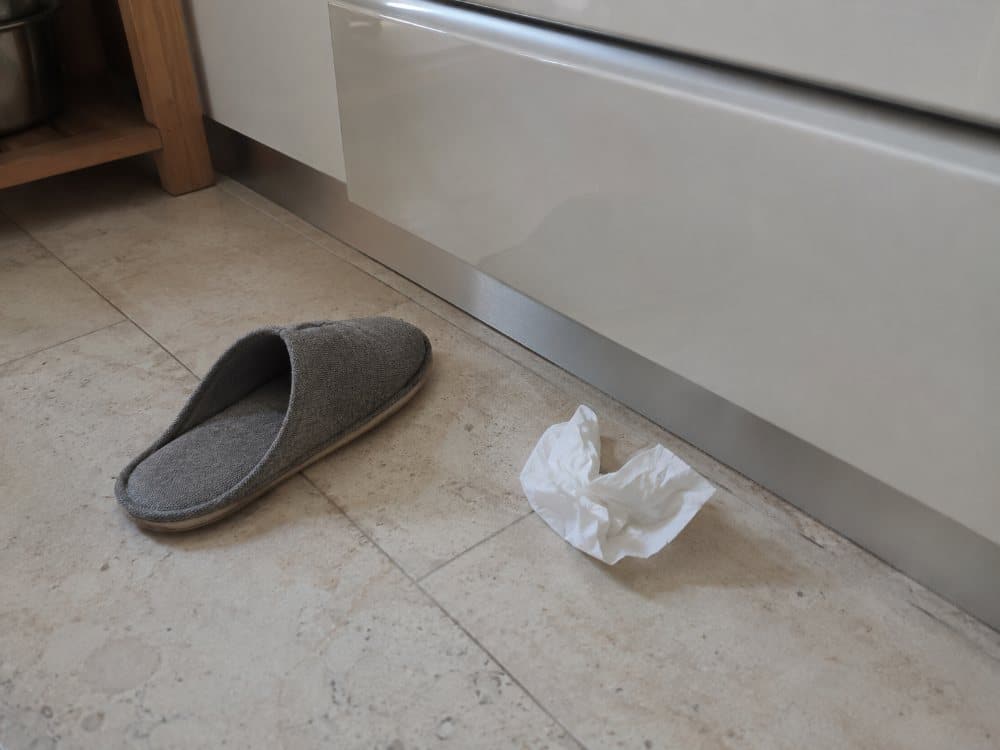 Hausschuh und Papiertaschentuch auf hellem Boden neben einem Küchenmöbelsockel