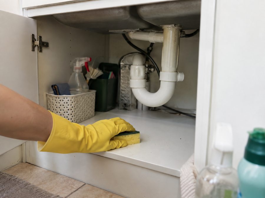 Hand mit Handschuh, die mit einem Schwamm das Tablar im Schrank unter der Spüle reinigt
